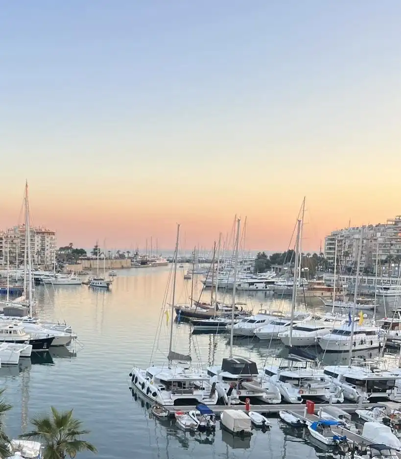 Sunrise over Pasalimani harbor in Piraeus with fishing boats and calm water.